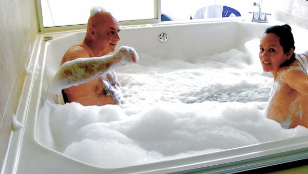 Slovakian woman and older man share a foamy nude bath in sunlit bathroom on girlsasian.net